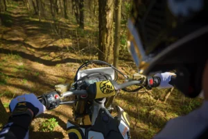 Sur-Ron Storm Bee Sur Ron Storm Bee electric dirt bike in motion on a forest trail, rider leaning into a turn, dust kicking up. Dynamic off-road action shot.